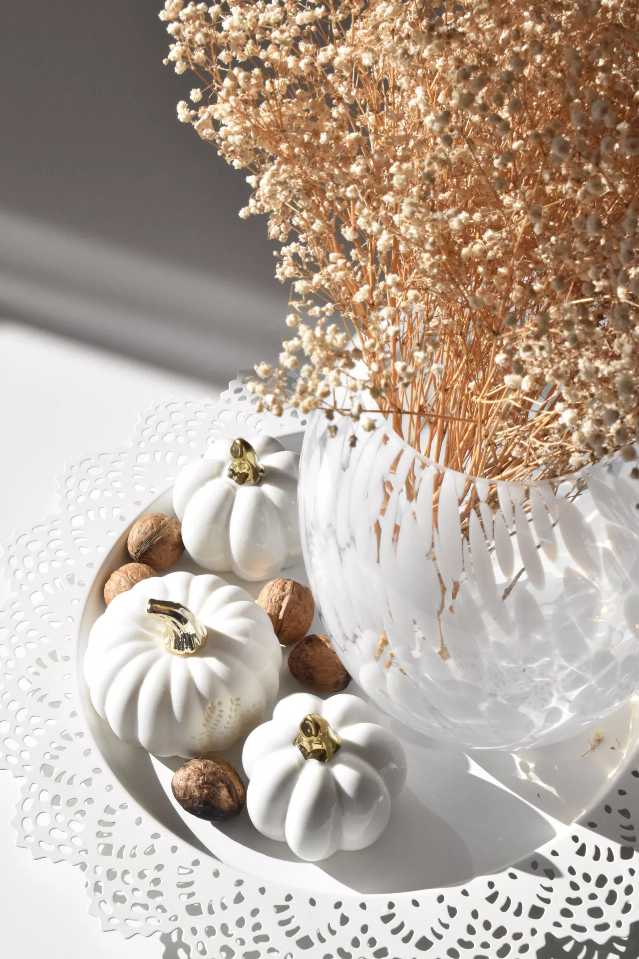 Fall living room decor ideas featuring dry flowers and white decor pumpkins with gold stems, arranged on a decorative white tray with walnuts and a clear glass vase.