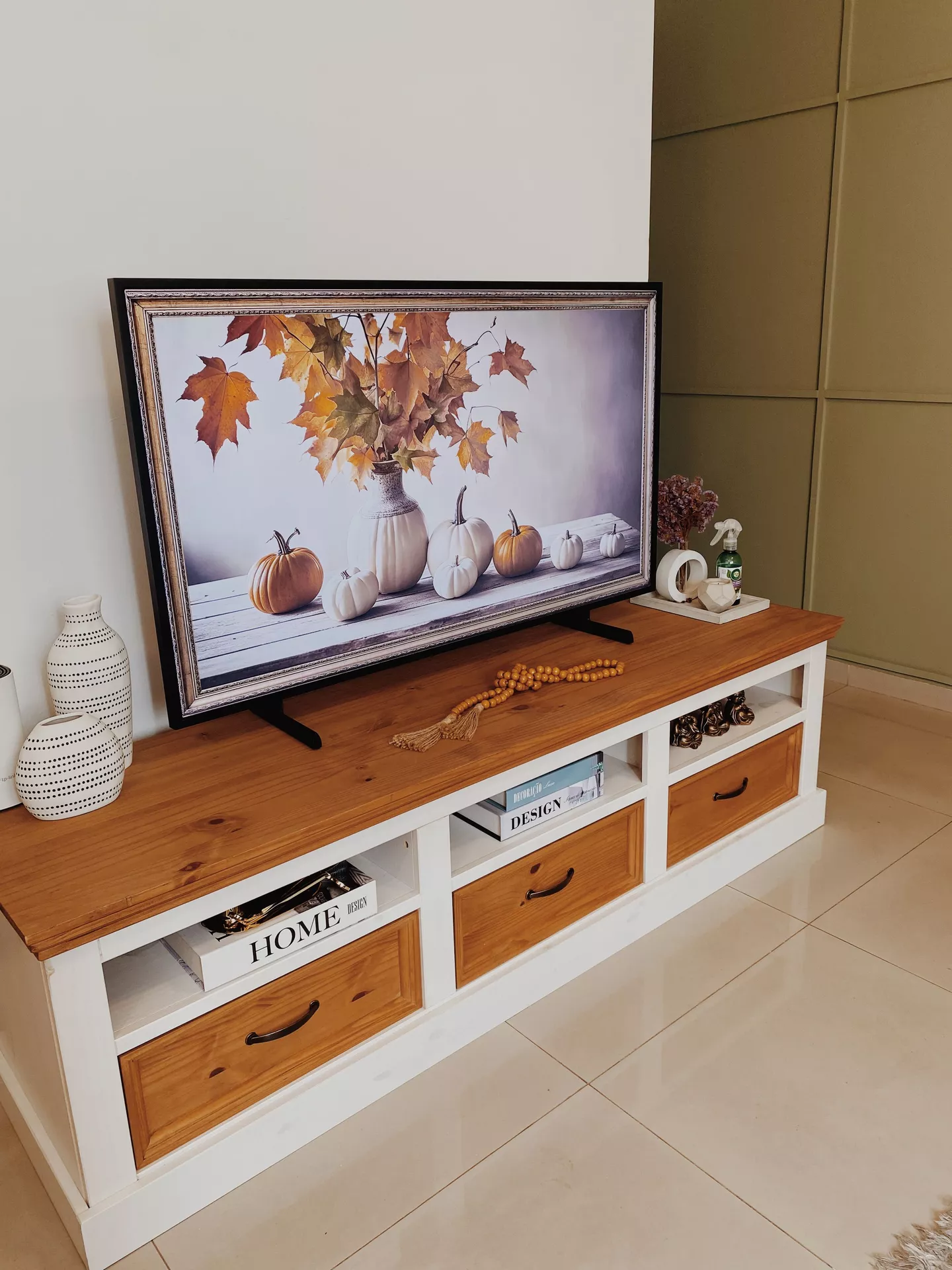 Fall living room decor ideas featuring a cozy fall TV background with pumpkins and autumn leaves, displayed on a wooden media console with neutral decorative accents.