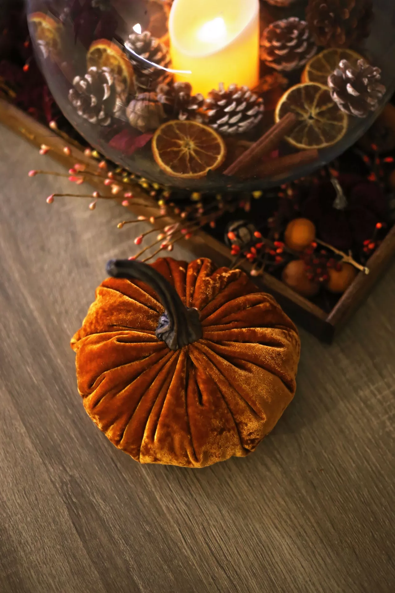 Fall living room decor ideas featuring a soft orange velvet pumpkin and autumn decor in glass jar with a glowing candle, pinecones, dried orange slices, cinnamon sticks, berries, and warm seasonal accents.