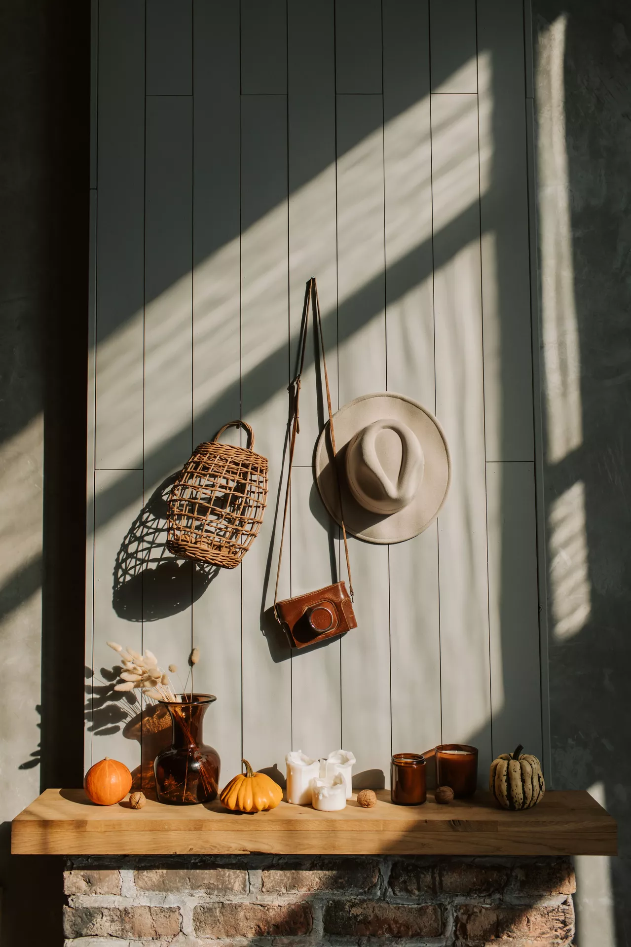Fall living room decor ideas featuring vintage fall decor with pumpkins, candles, an amber glass vase, a woven basket, vintage camera, and neutral hat styled around a rustic fireplace mantel.