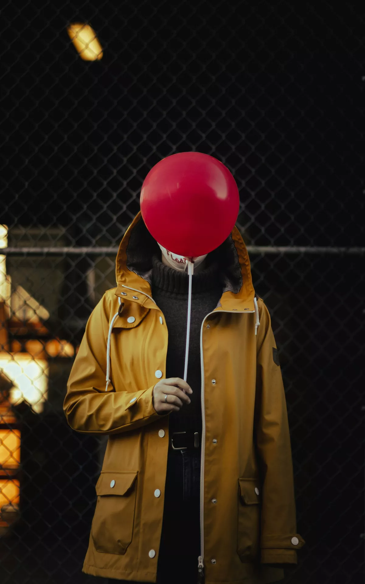 Halloween costume ideas inspired by It from Stephen King, featuring a person in a yellow raincoat holding a bright red balloon in front of their face against a dark, eerie background.