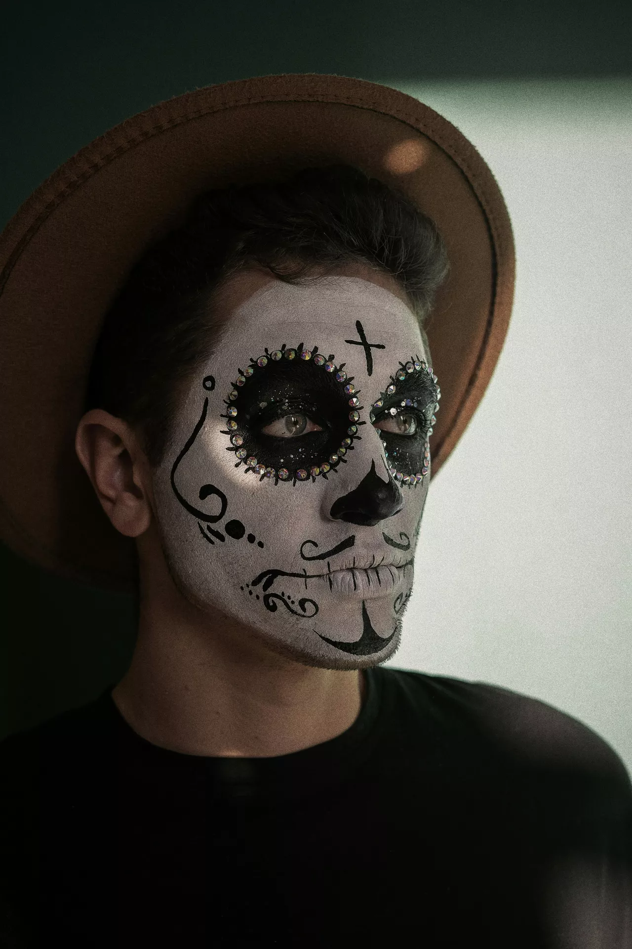 Halloween costume ideas featuring a sugar skull mask look with white face paint, black decorative details, rhinestones around the eyes, and a wide brown hat.