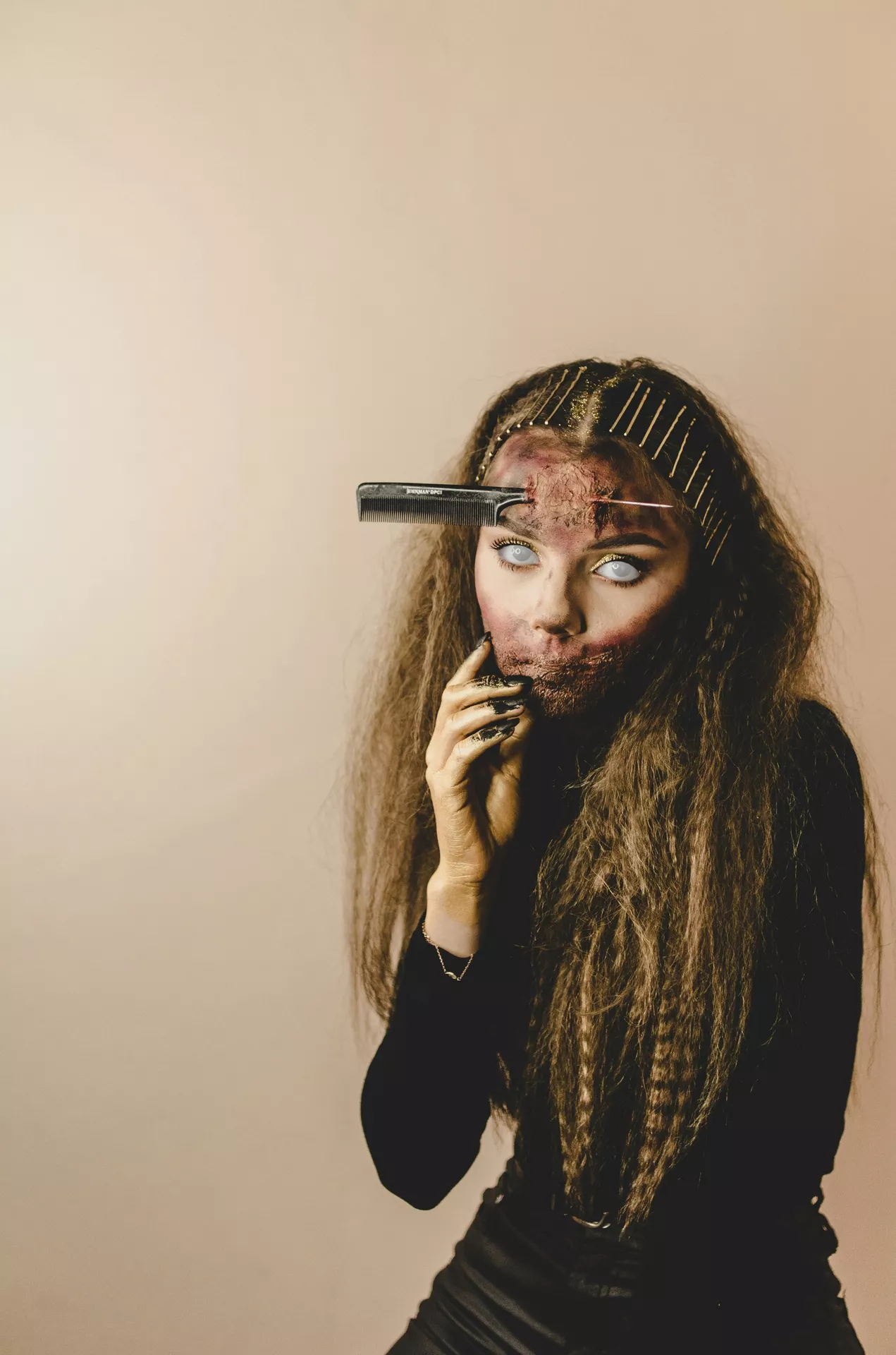 Halloween costume ideas featuring a zombie hairdresser with eerie white contact lenses, scarred makeup, messy crimped hair, hairpins, and a comb appearing to pierce her forehead.