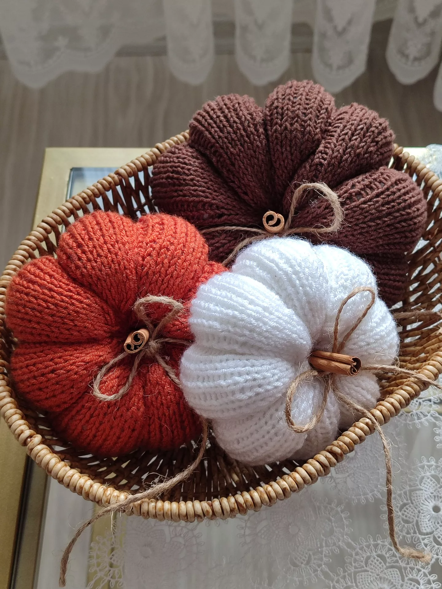 DIY autumn craft ideas featuring three Crocheted Pumpkins in warm brown, burnt orange, and white yarn, decorated with rustic twine bows and cinnamon stick stems in a woven basket.