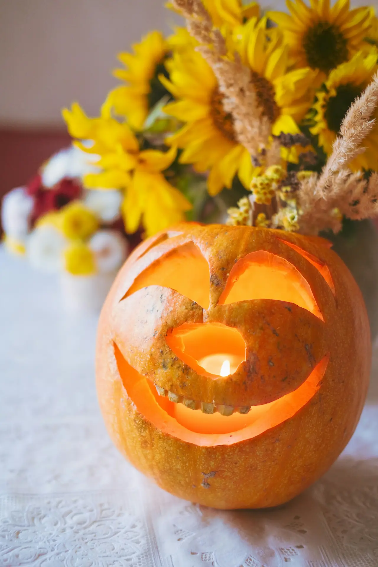 Pumpkin carving ideas featuring a glowing jack-o-lantern with a happy face with teeth, curved eyes, raised eyebrows, and a wide cheerful smile, displayed in front of bright yellow sunflowers.
