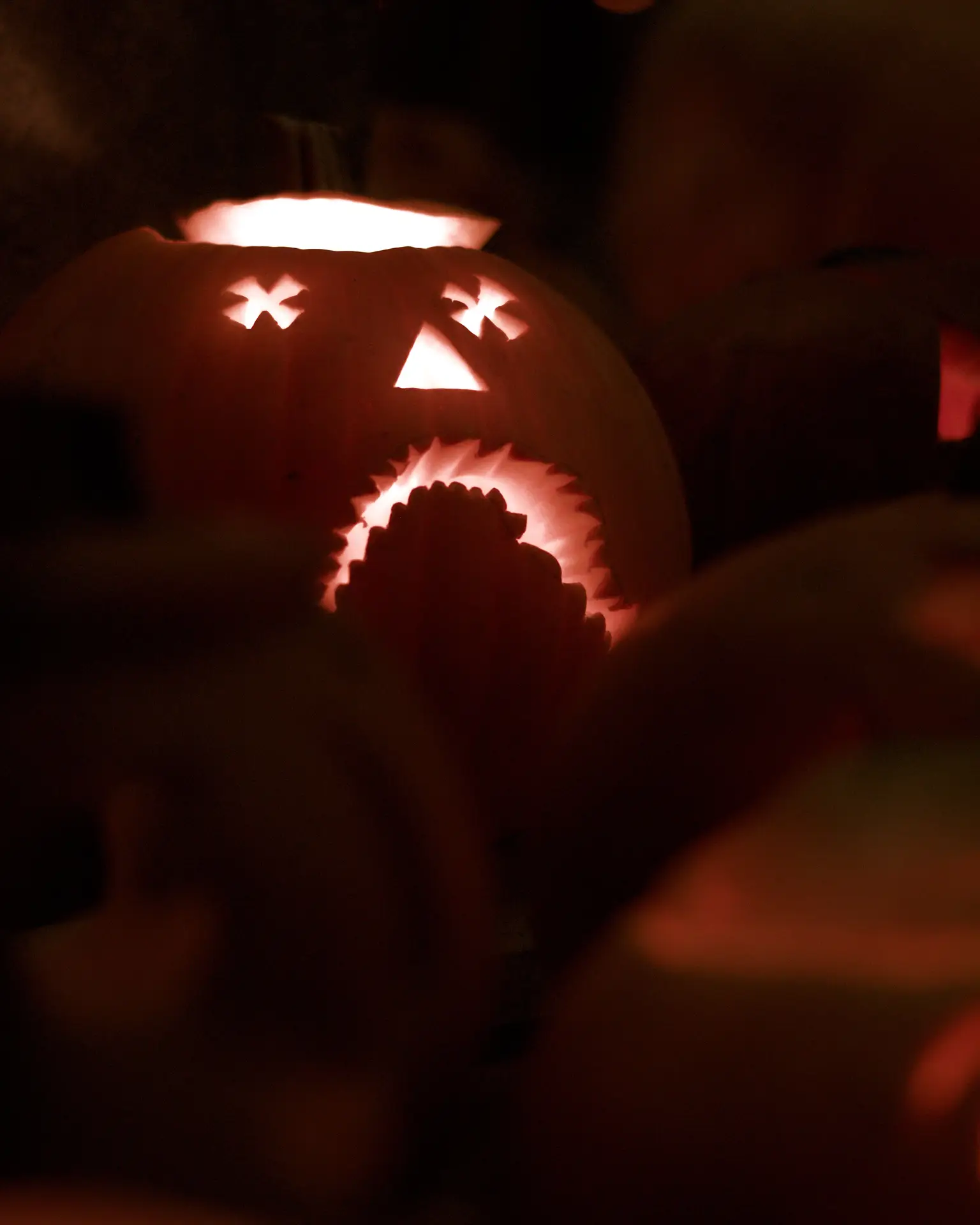 Pumpkin carving ideas featuring a glowing jack-o-lantern with a sad face, X-shaped eyes, a triangular nose, and a large downturned jagged mouth illuminated in the dark.