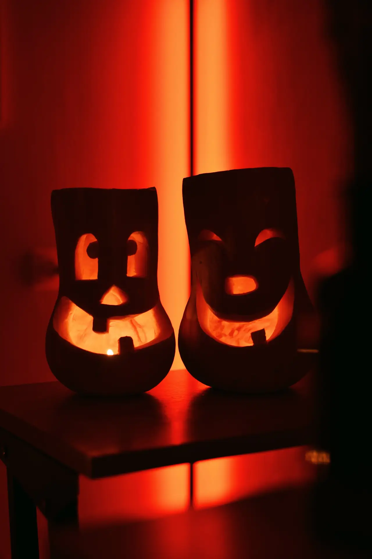 Pumpkin carving ideas featuring two smiling pumpkins with cheerful carved faces, glowing warmly side by side in a dark room with atmospheric orange lighting.